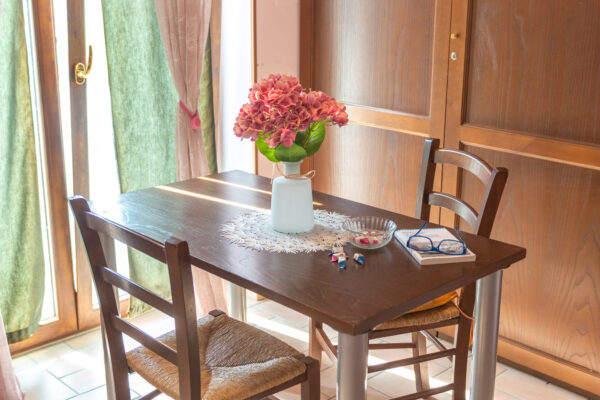 Tavolino in legno con sedie e vaso di fiori accanto alla portafinestra della Camera Colle della Collina del Nido del Falco