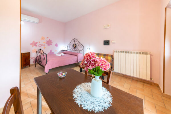 Tavolo con vaso di fiori in primo piano e letto matrimoniale sullo sfondo nella Camera Colle della Collina del Nido del Falco a Montefalco
