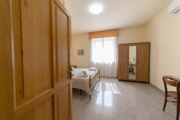 Camera Verde Ulivo vista dall’ingresso con porta in legno in primo piano