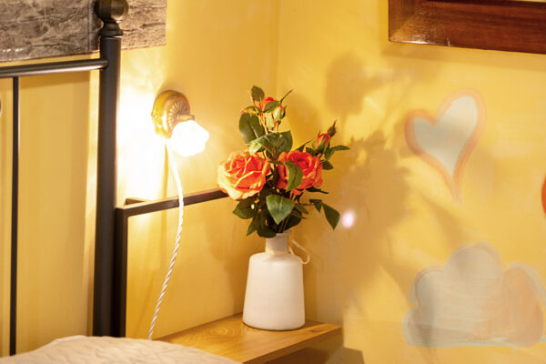 Comodino con lampada e fiori accanto al letto della Camera Colle del Sole