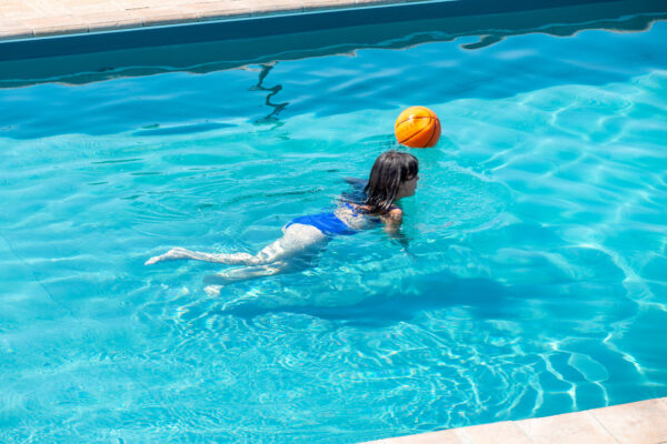 Bambina che gioca con un pallone arancione nella piscina del Nido del Falco a Montefalco