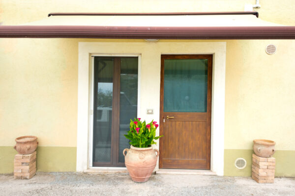 Ingresso esterno del Nido del Falco con porta in legno e vaso di fiori